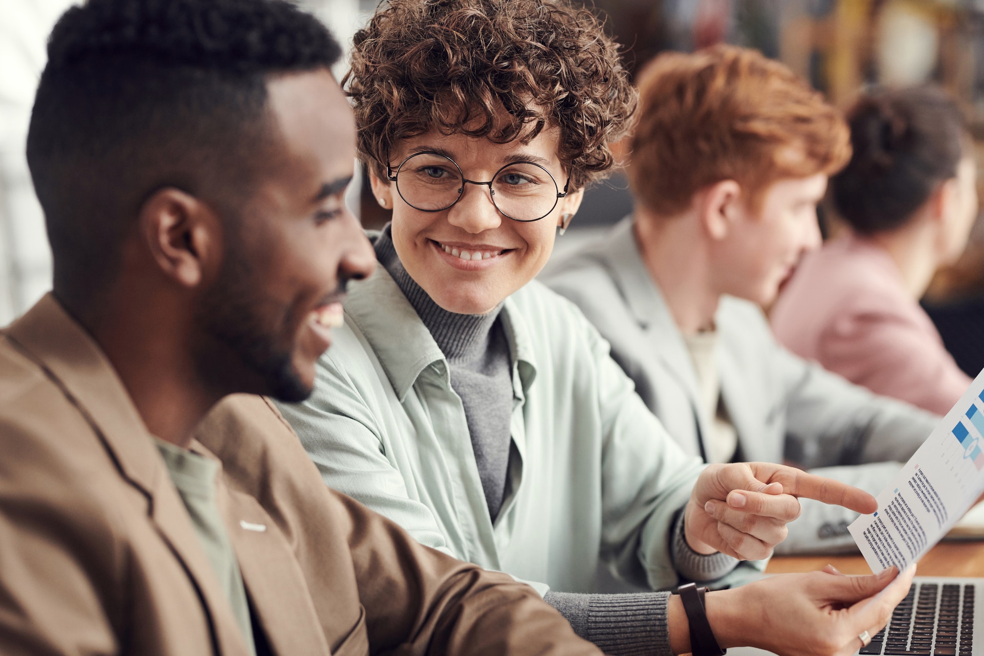 four-people-sitting-desk woman smiling at man discussing supervisor evaluation