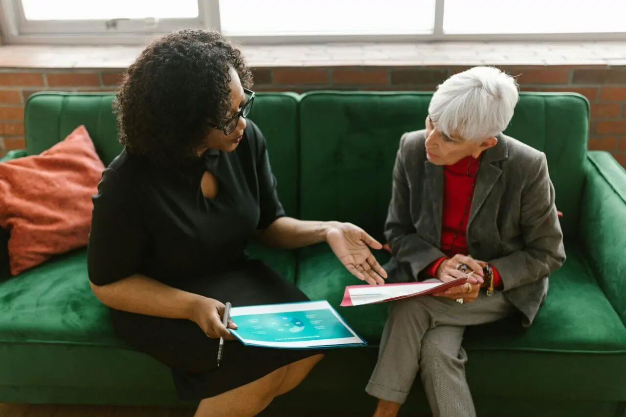 black-woman-and-older-woman-talking-on-sofa-looking-at-papers two women colleagues discussing strategies to combat a toxic workplace